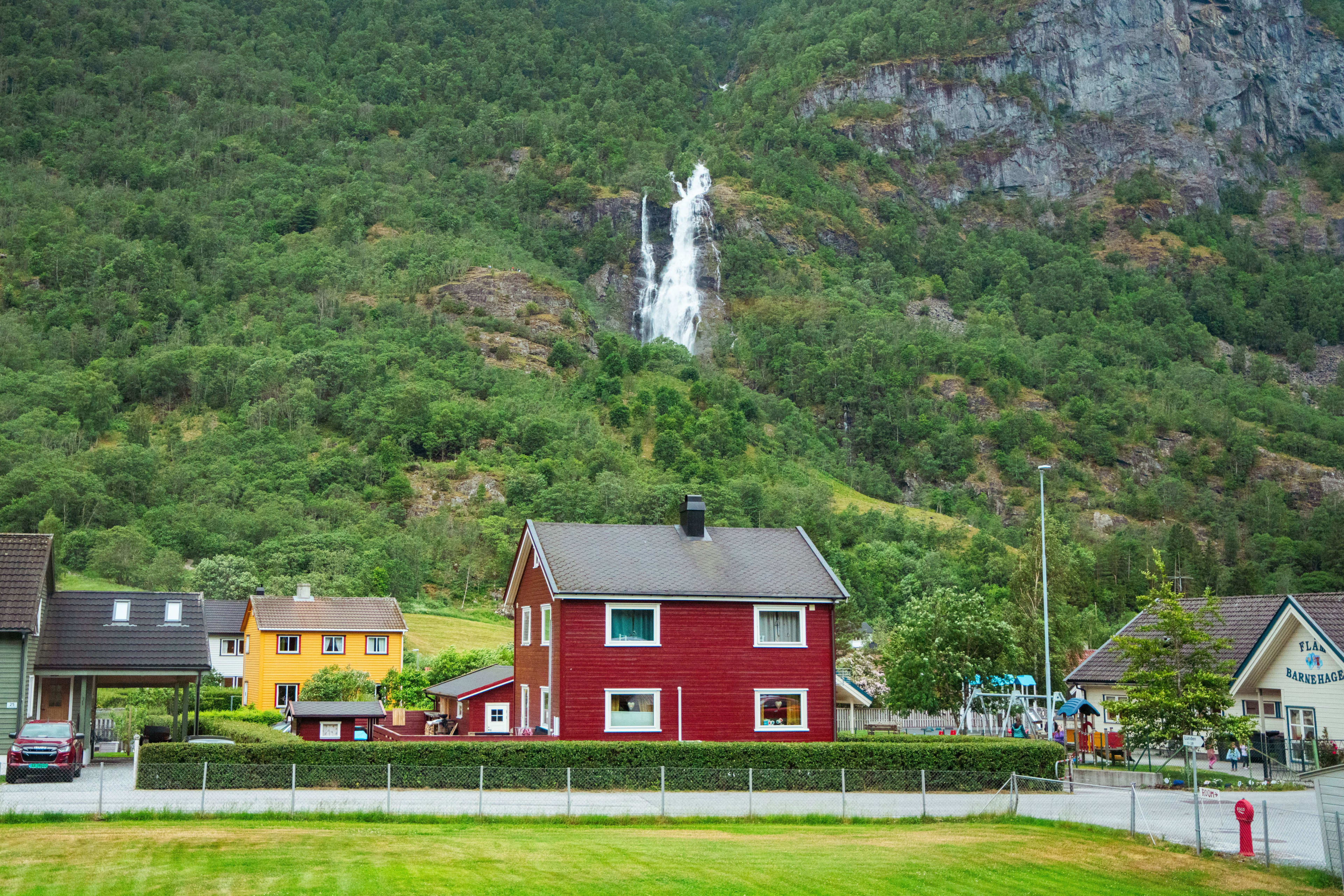 Colorful houses and kindergarten at mountain base with tall waterfall behind.
