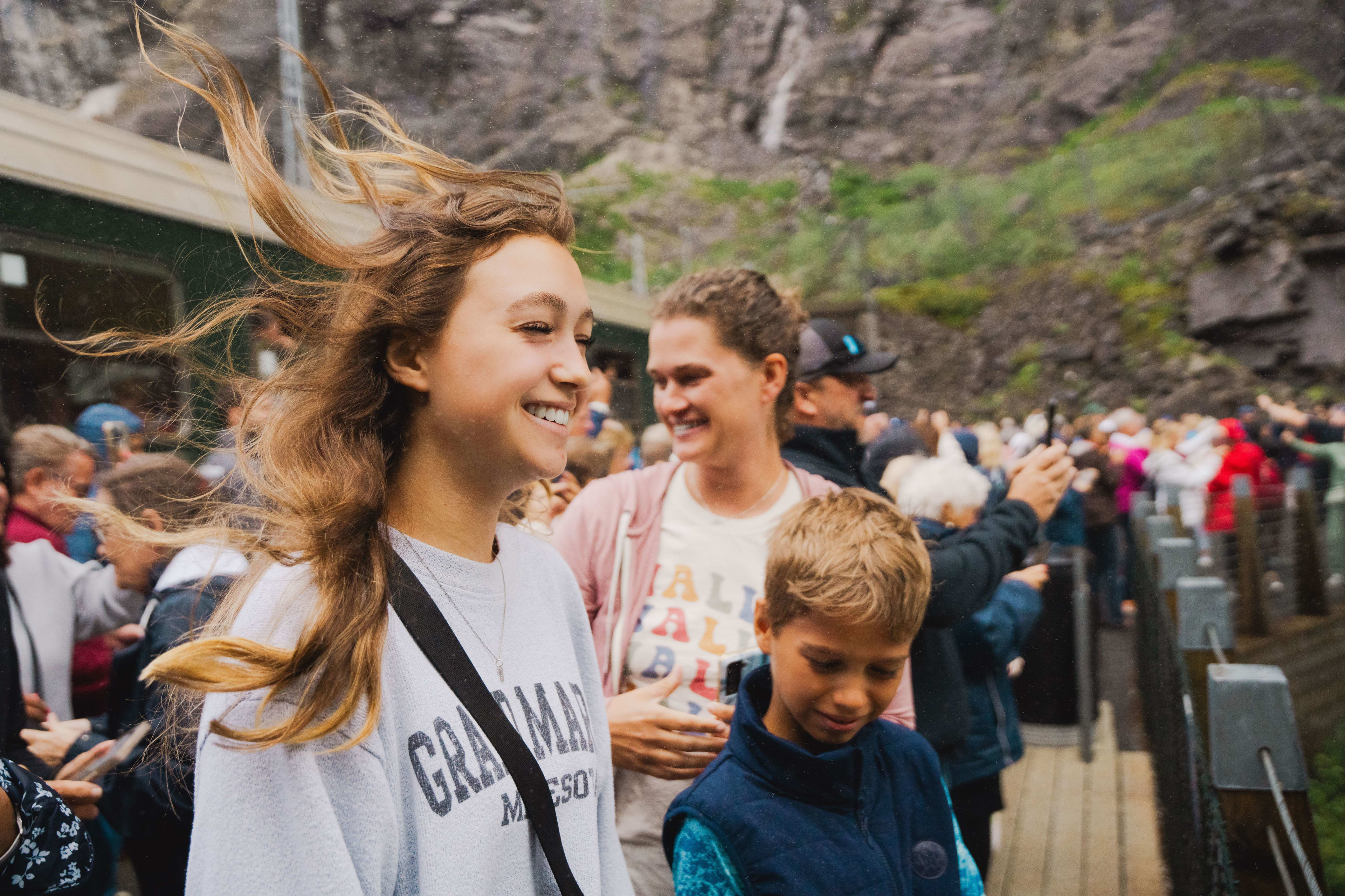 Smiling girl with messy hair stands on wooden platform among cheerful crowd.