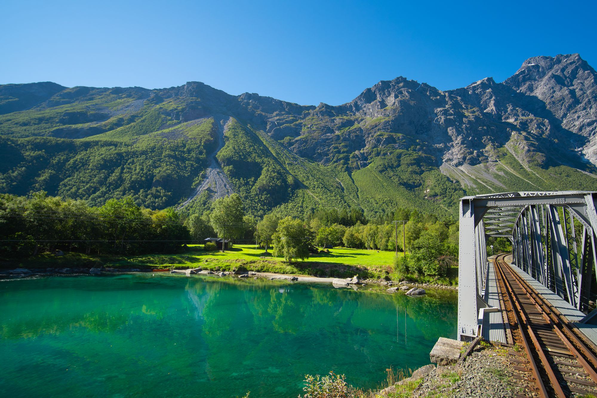 En stålgjennomgangsbane som går over en turkis elv, med dramatiske fjell i bakgrunnen.