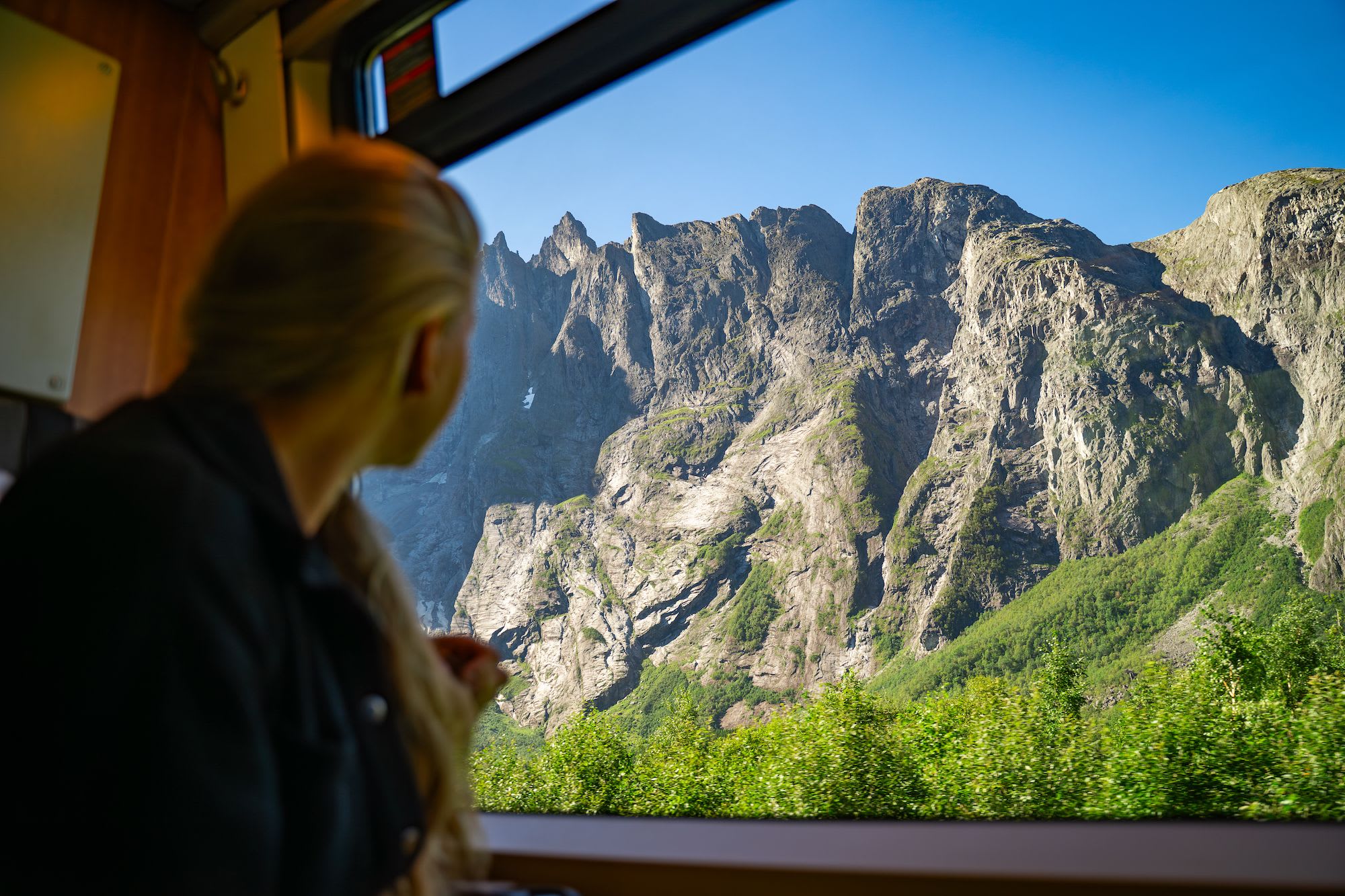 En person i et tog som ser på de tårnende fjellene utenfor vinduet, og fanger den fantastiske utsikten med telefonen.