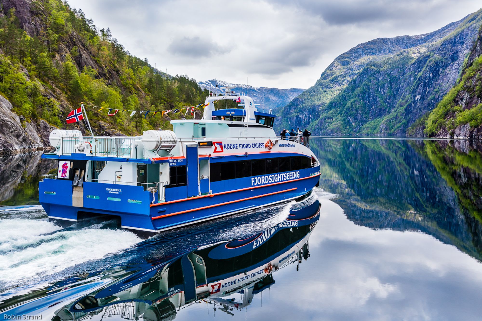Colorful fjord boat on calm water with mountain reflections.