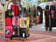 Colorful suitcases stacked on hotel luggage carts, hotel worker arranging bags near cars.
