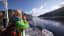 Woman takes photo from deck on the Lysefjord cruise boat surrounded by cliffs, blue sky, and calm water