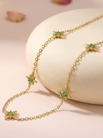 Collier doré à motifs étoiles serties de zircons verts, présenté sur un socle crème