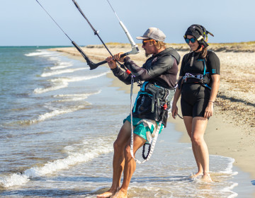 Kitesurf instructor explaining kite control to a student with radio helmet
