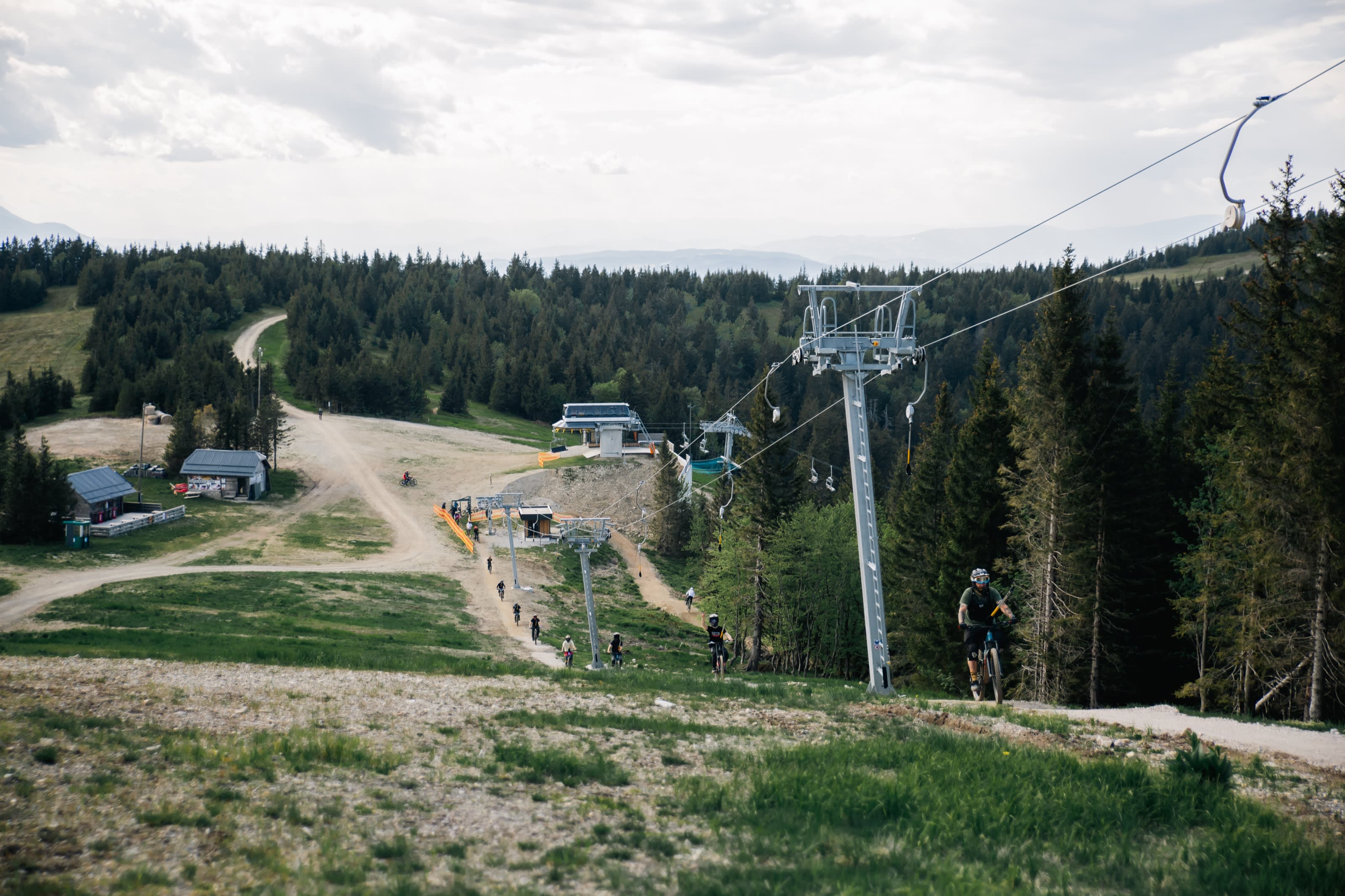 Kolesarji na progi ob sedežnici, v ozadju gozd in Pohorje