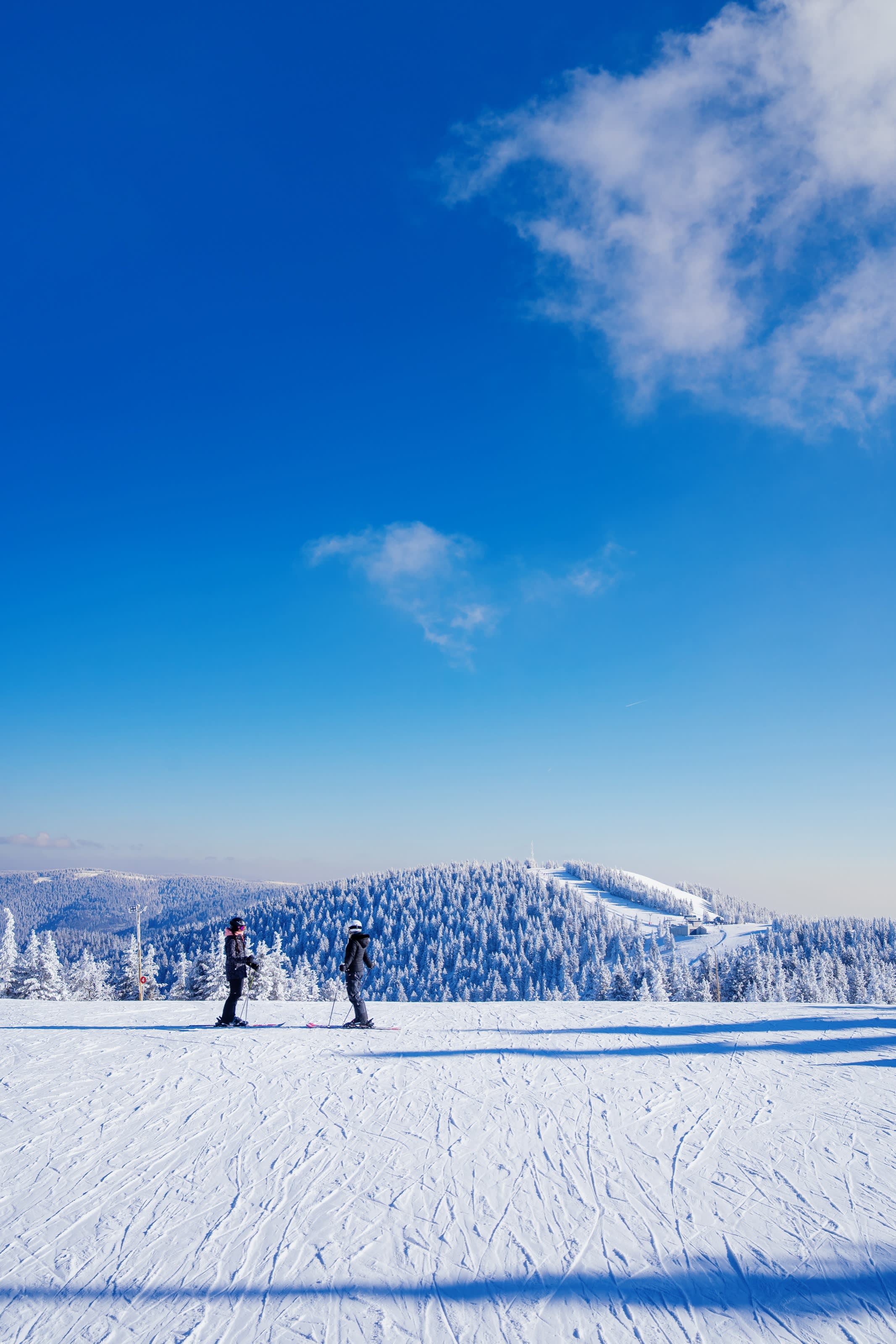 Smučarja na urejeni progi z razgledom na Pohorje