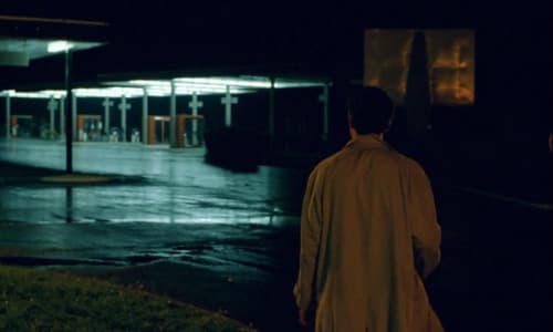 A man stands looking at an empty gas station in the dark.