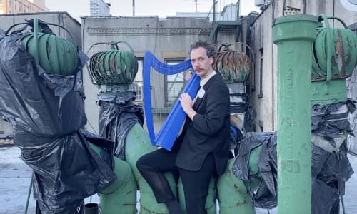 Tom CJ Brown wearing a suit playing a bright blue harp.