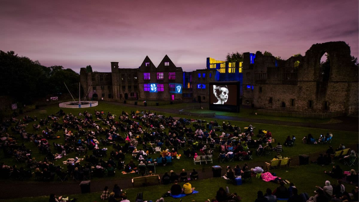 A large audience watching Bride of Frankenstein at Dudley Castle - the castle is lit up with coloured lights and projections either side of the screen.