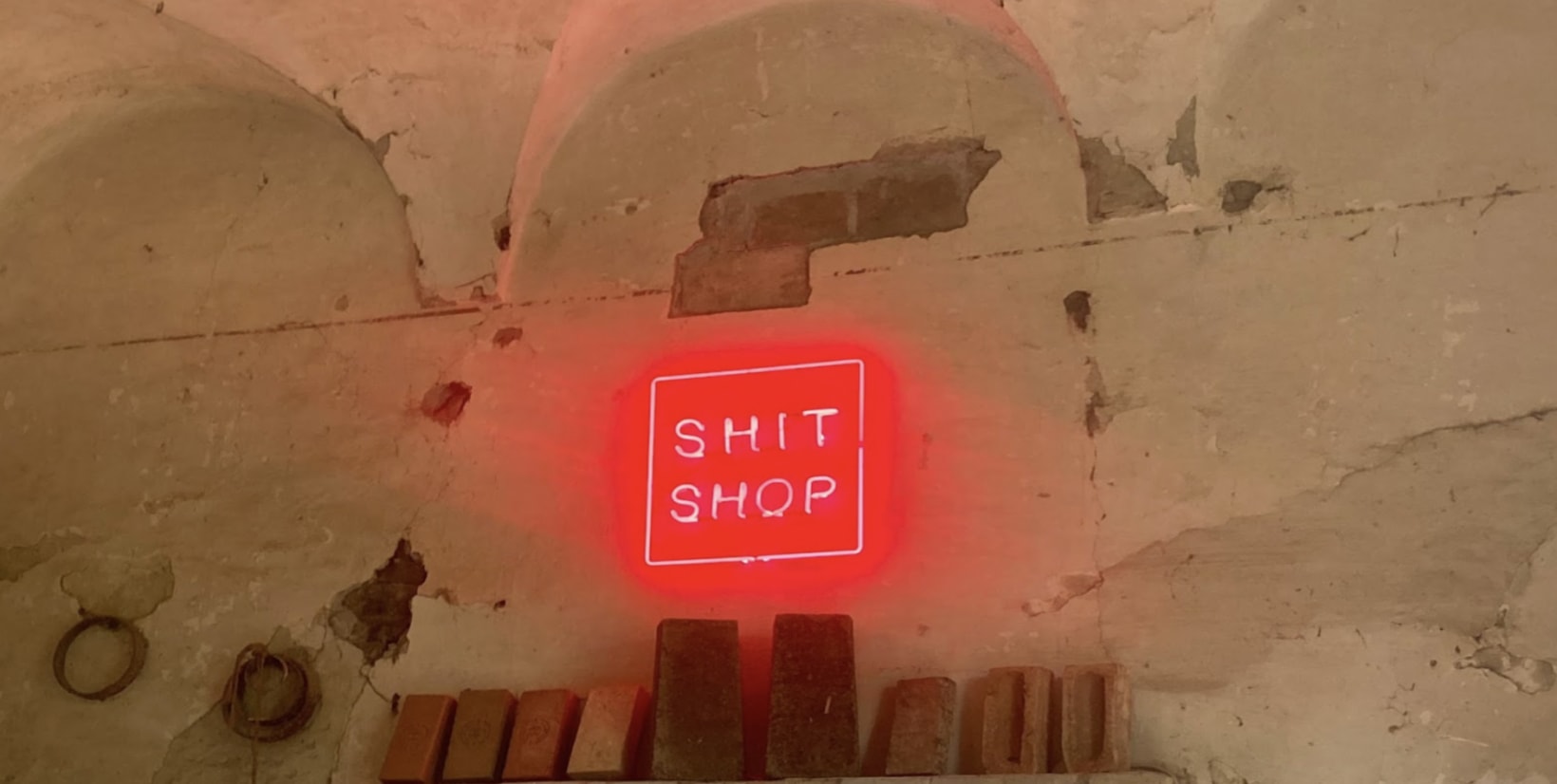 A red neon sign saying Shit Shop