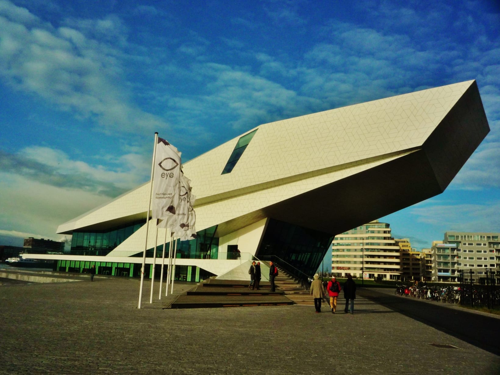 Photograph of the Eye Filmmuseum, against a blue sky. People walk towards the building.