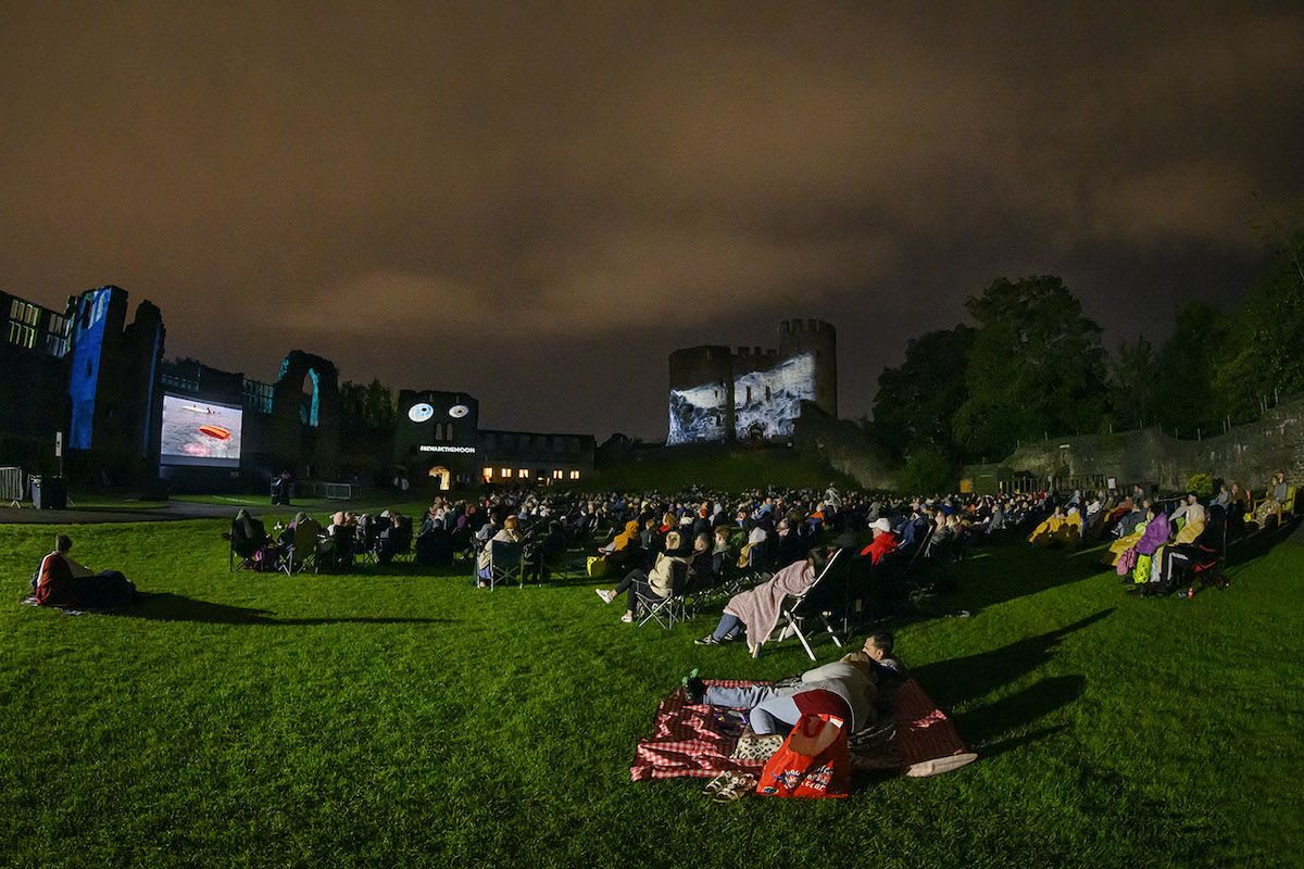 Outdoor cinema at Dudley Castle. People sat on chairs and picnic blankets with the pop up cinema screen surrounded by the castle ruins. 