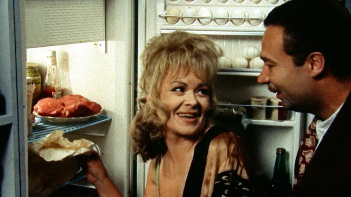 Characters Ona (Jirina Bohdalová) and Bohouš (Vladimír Mensík) laughing as Ona reaches into a well stocked fridge