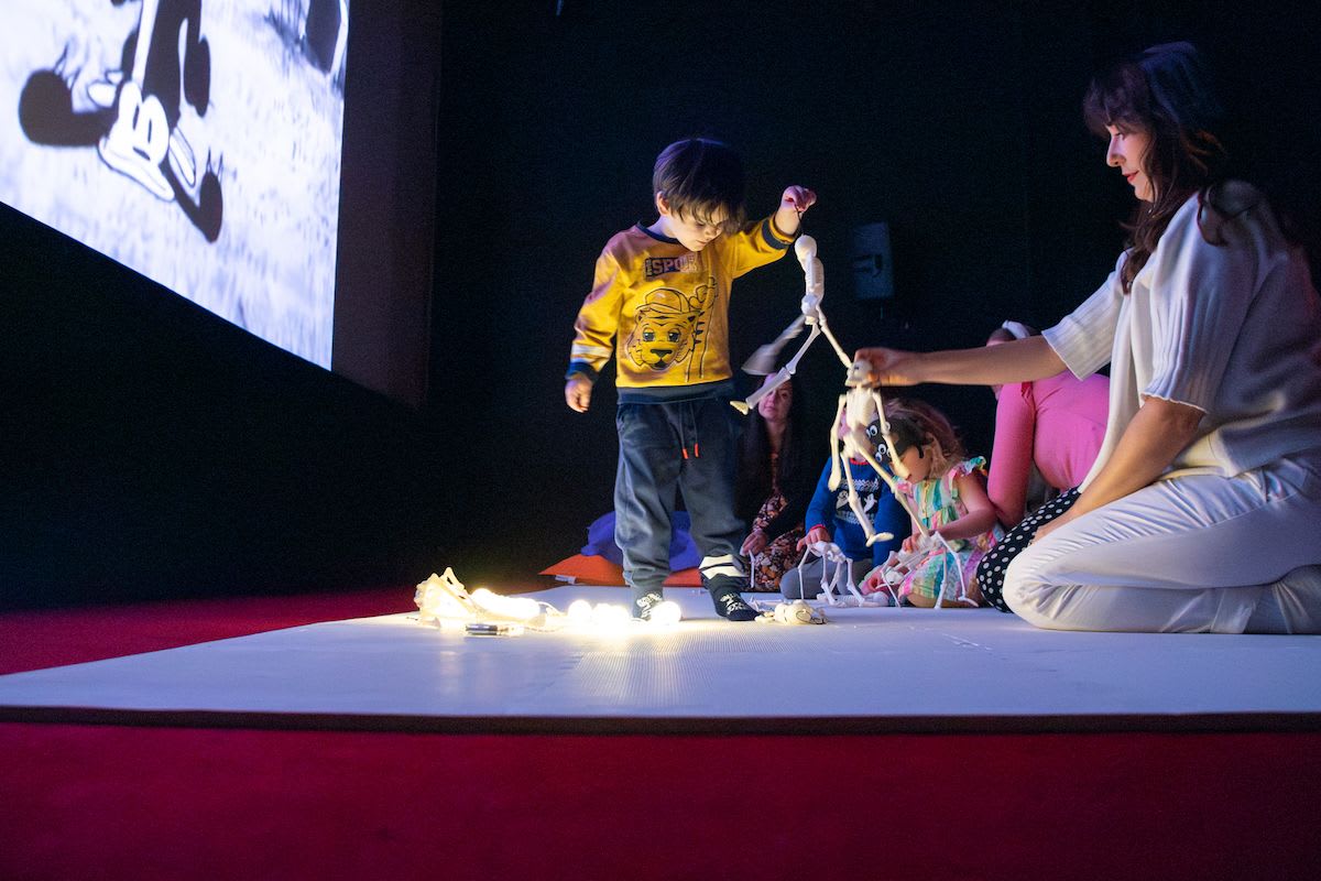 A child playing with plastic skeletons, a pop up cinema screen in the background and fairy lights on the floor. 