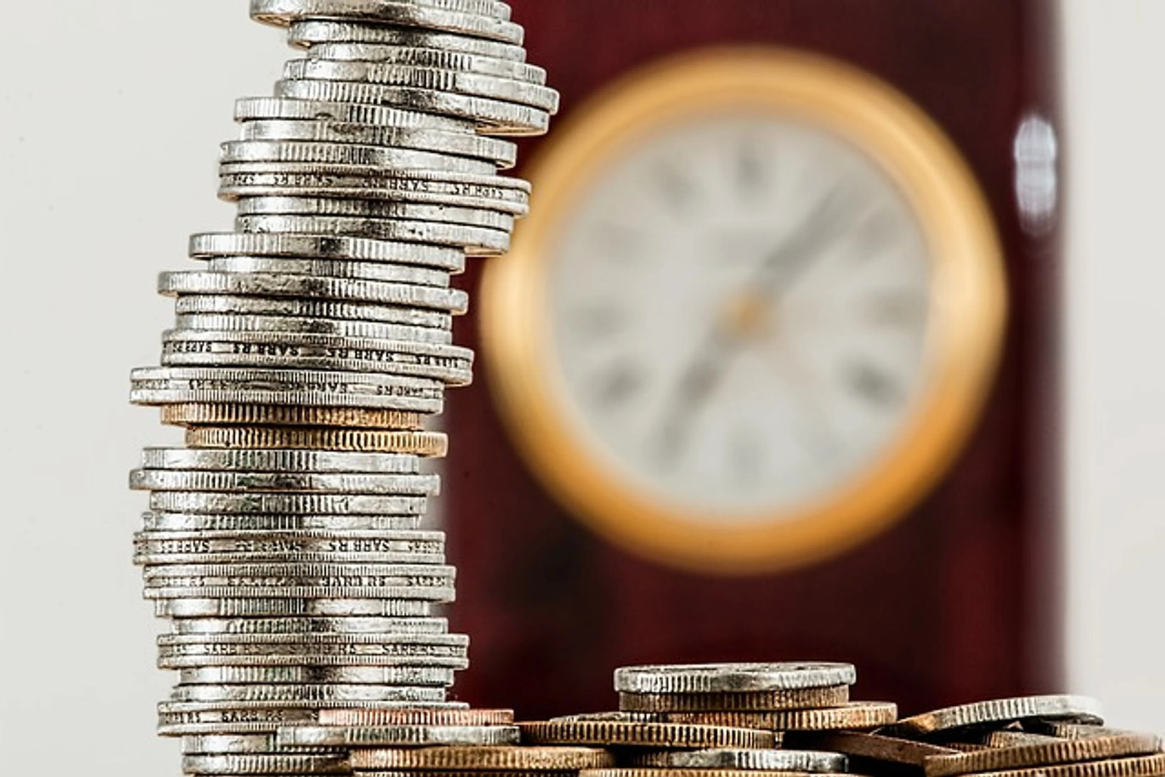 Coins stacked on top of one another, with a ticking clock in the background.