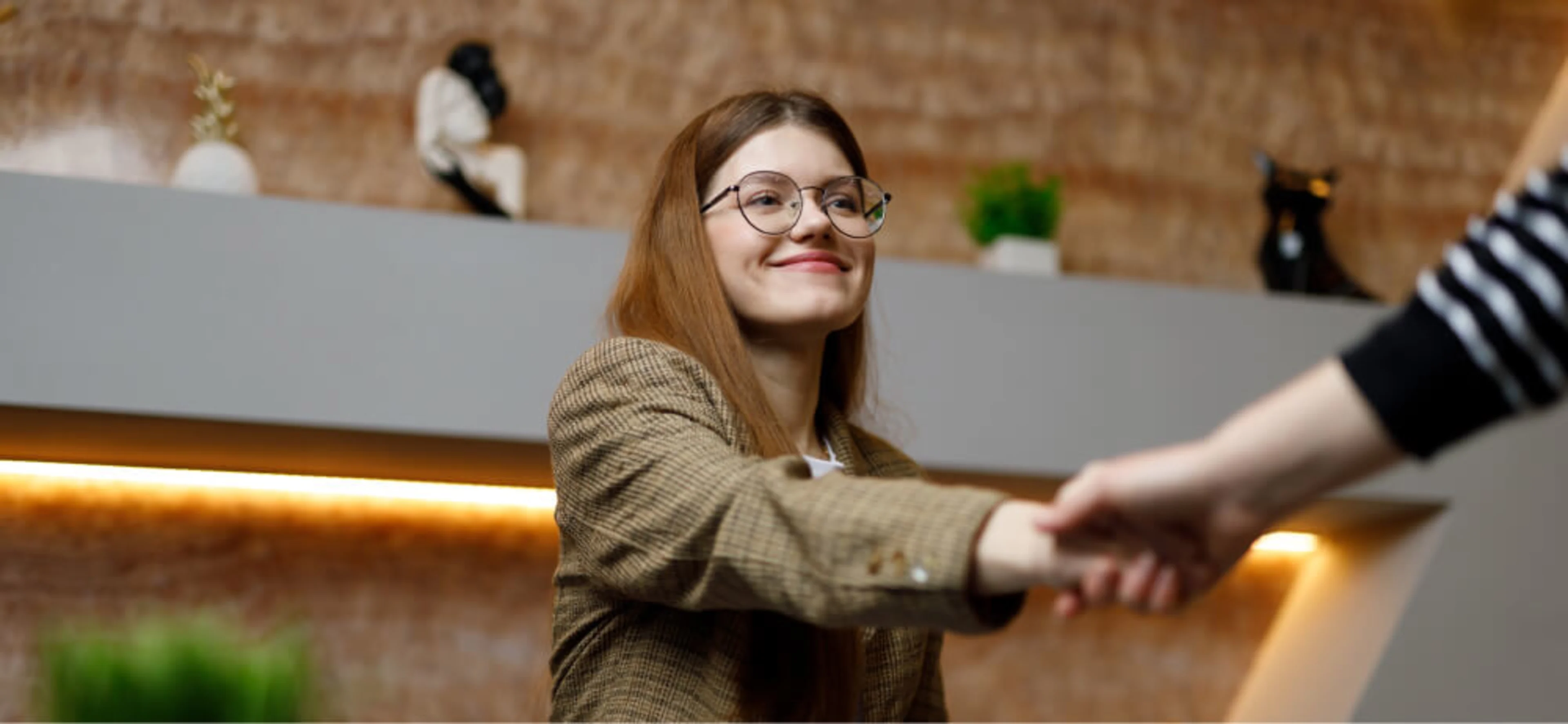 A young woman dressed in formal attire engaging in a handshake with the interviewer during a job interview