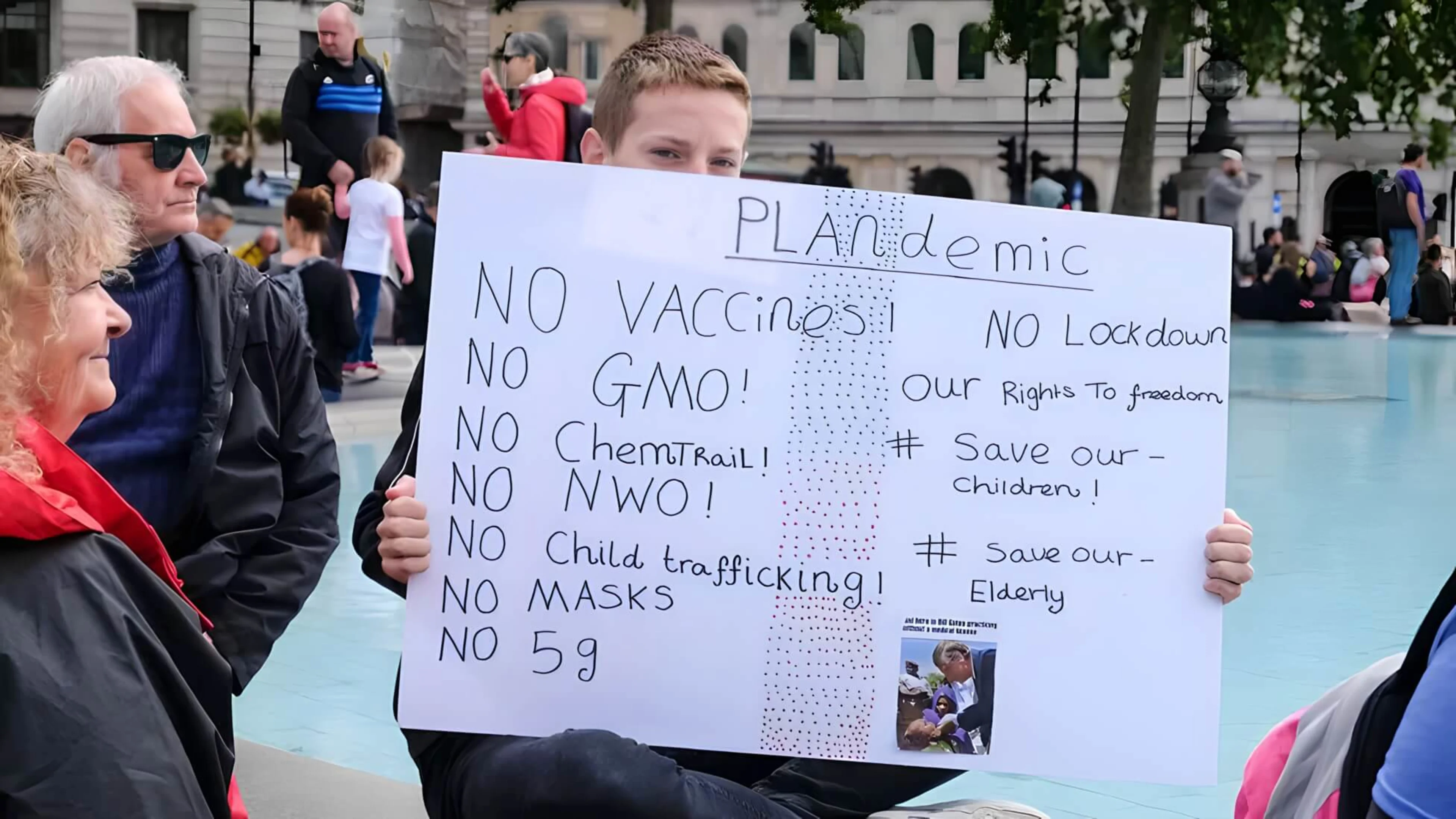 A young protester holds up a sign about the “Plandemic” and other conspiracy theories