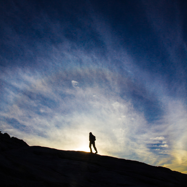 "woman walking on mountain silouhetted by sunrise or sunset" stock image