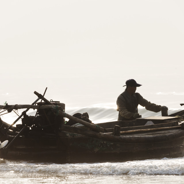 "Fisherman in China bringing his wooden boat to moore on the beach in China" stock image