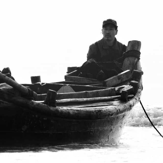 "Chinese fisherman wading in the shallows of the beach to moore his wooden fishing boat" stock image