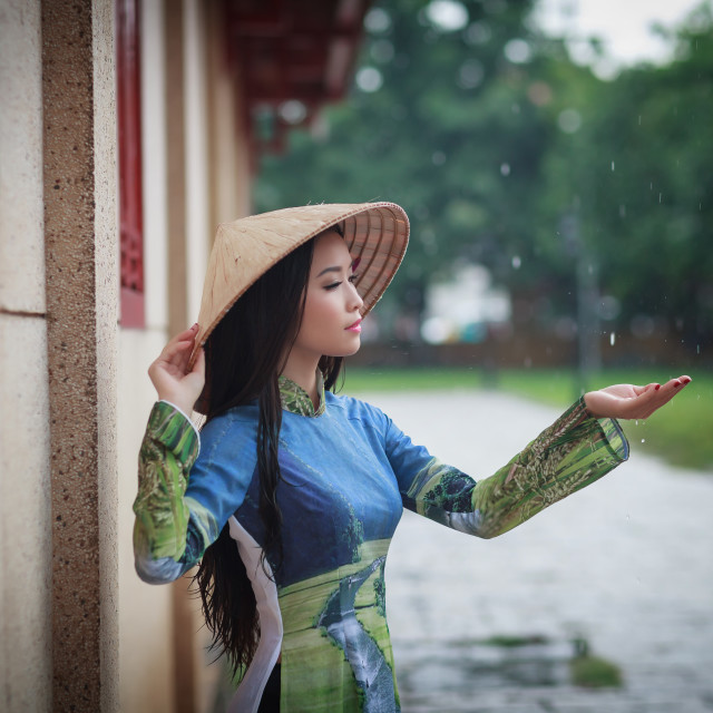 Vietnamese women wear Ao dai holding umbrella in the rain. Ao dai is ...