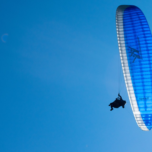 "Paraglider flying in bright blue sky" stock image