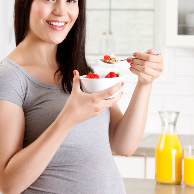 "Pregnant woman eating healthy breakfast of granola and strawberries" stock image