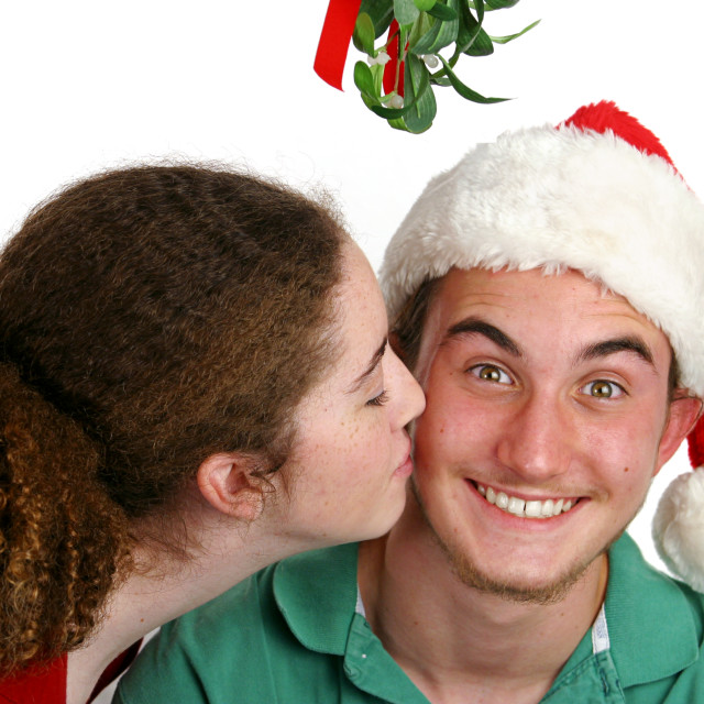 A teen girl kissing a very surprised boy under the mistletoe.. 