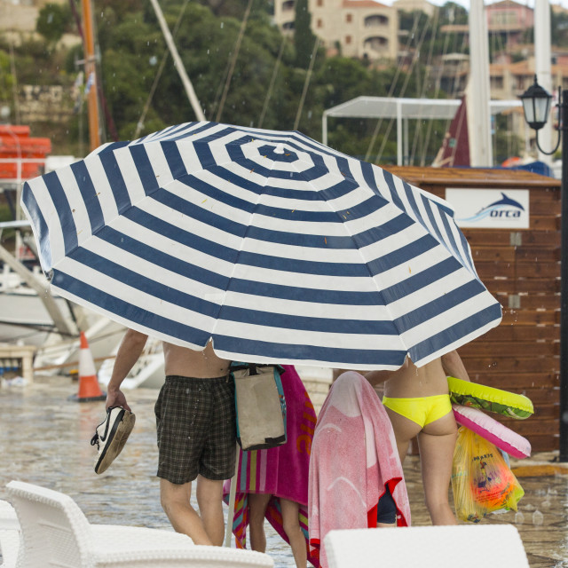 "A family use a large beach umbrella to escape torrential rain and hail from a..." stock image