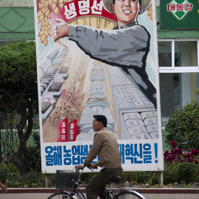 "North Korean man riding a bicycle in front of a propaganda billboard..." stock image