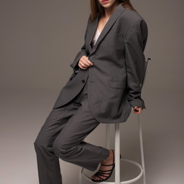 "Young girl model in gray man suit sitting on chair in studio" stock image
