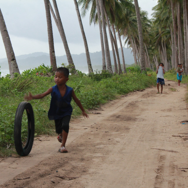 "Child pushes tyre on Long Beach, Philippines" stock image