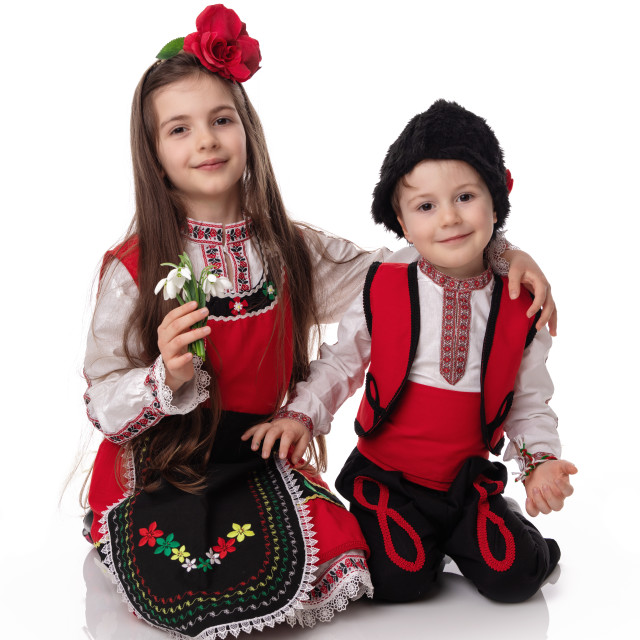 "Bulgarian kids boy and girl in traditional folklore costumes with spring flowers snowdrop and handcraft wool bracelet martenitsa symbol of Baba Marta" stock image