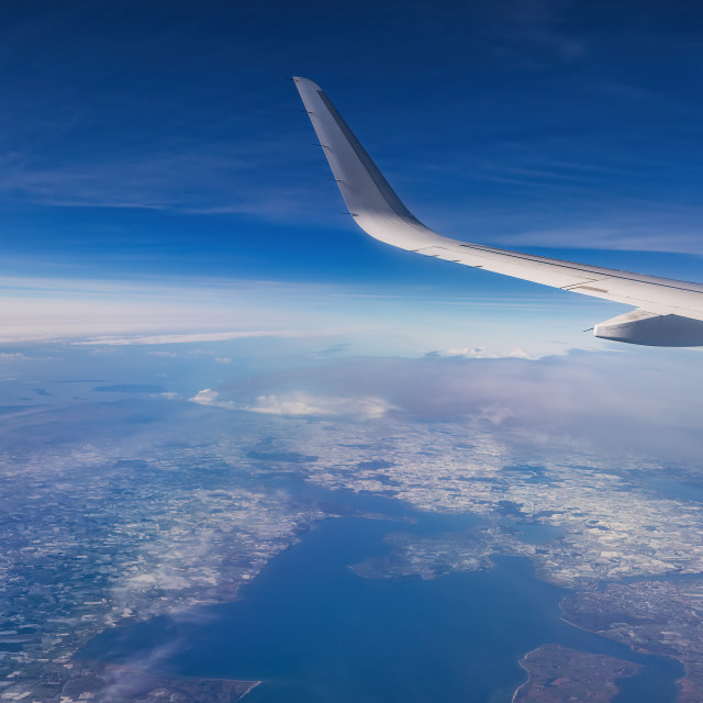 "Airplane flying above snowy mountains landscape on a sunny day, view from plane window of clouds and wing turbines" stock image