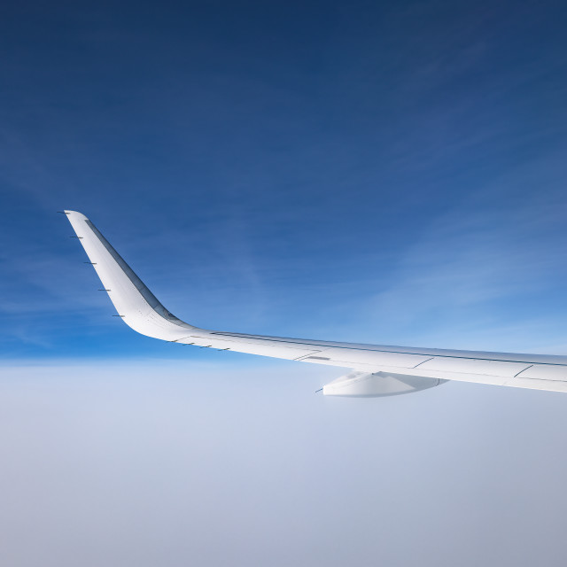 "Airplane flying above snowy mountains landscape on a sunny day, view from plane window of clouds and wing turbines" stock image