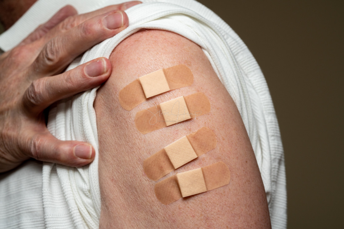 "Senior man holding up shirt showing four covid-19 vaccine injections" stock image