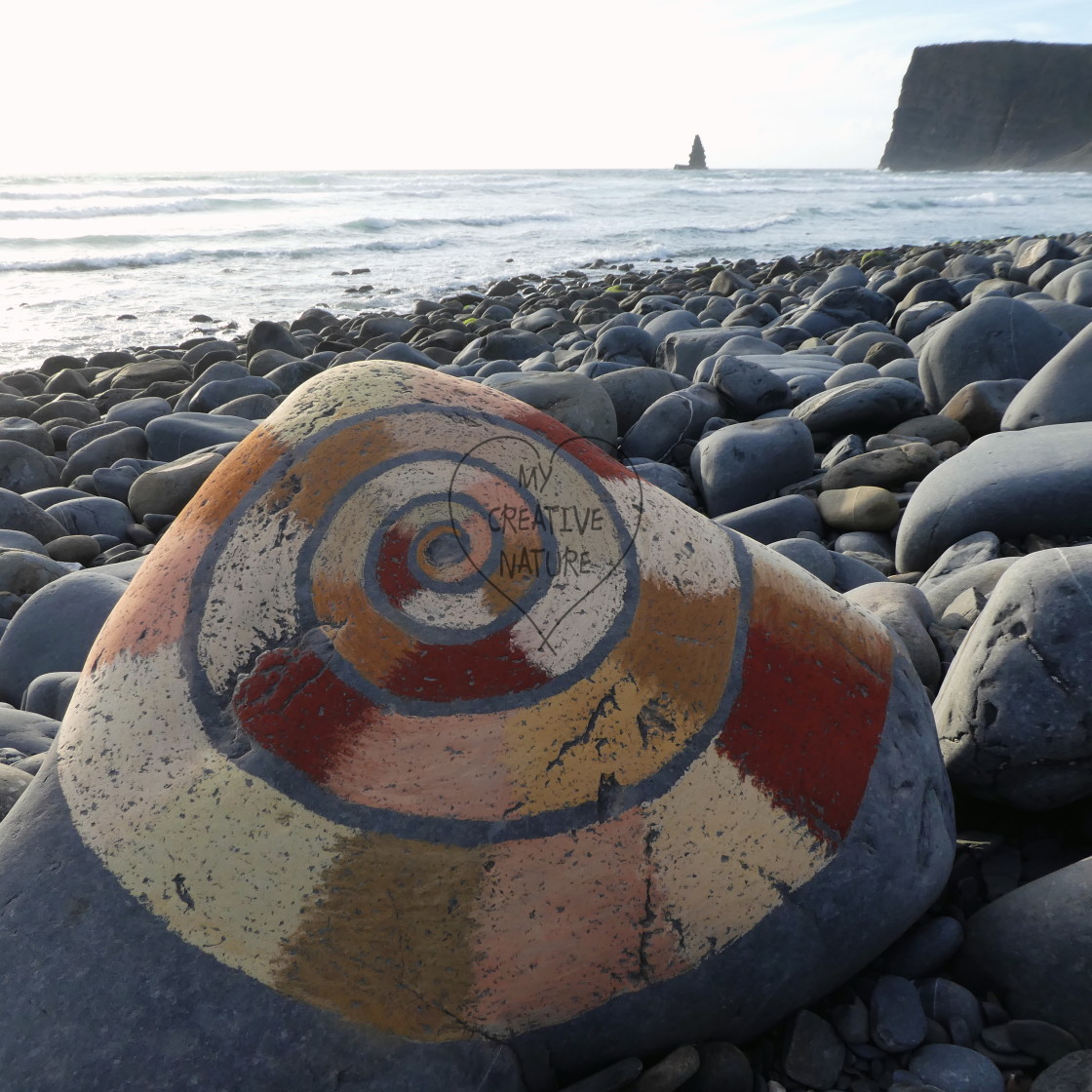 "spiral painted with stones on a beach rock with view on arrifana needle rock" stock image