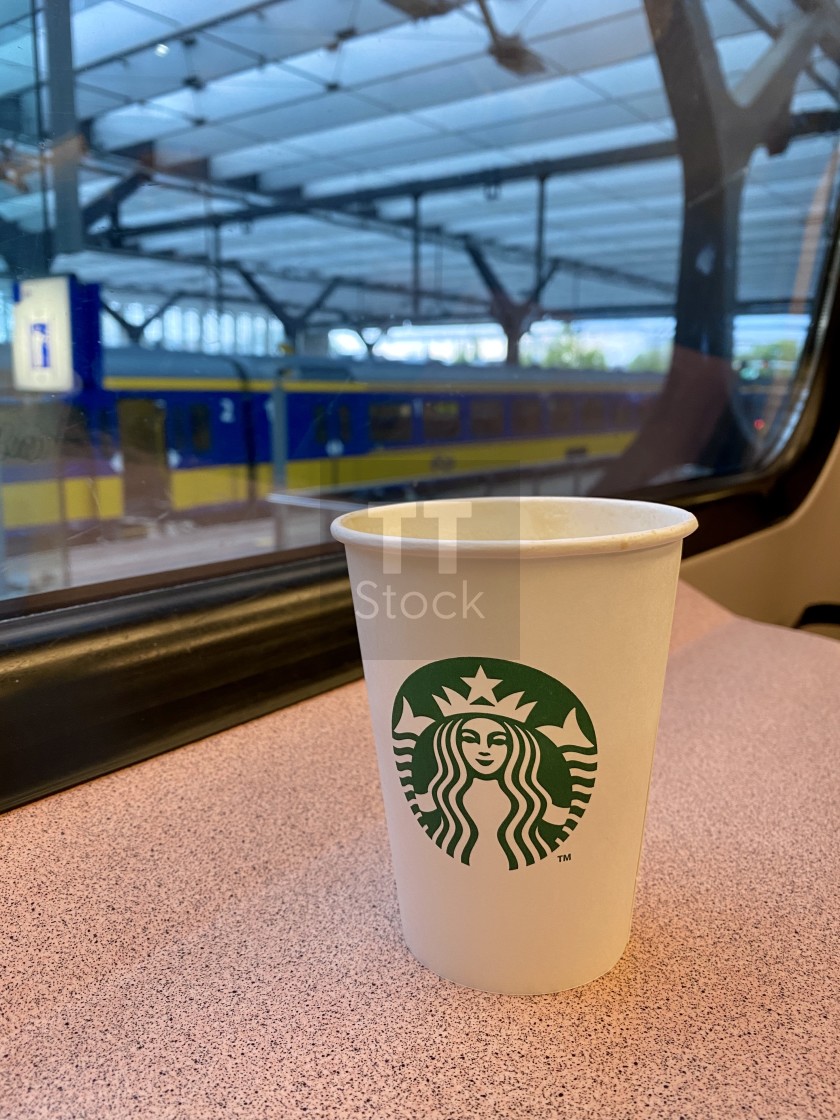 "Coffee to go commuting to work on train. Starbucks in carton cup. Train station through window." stock image