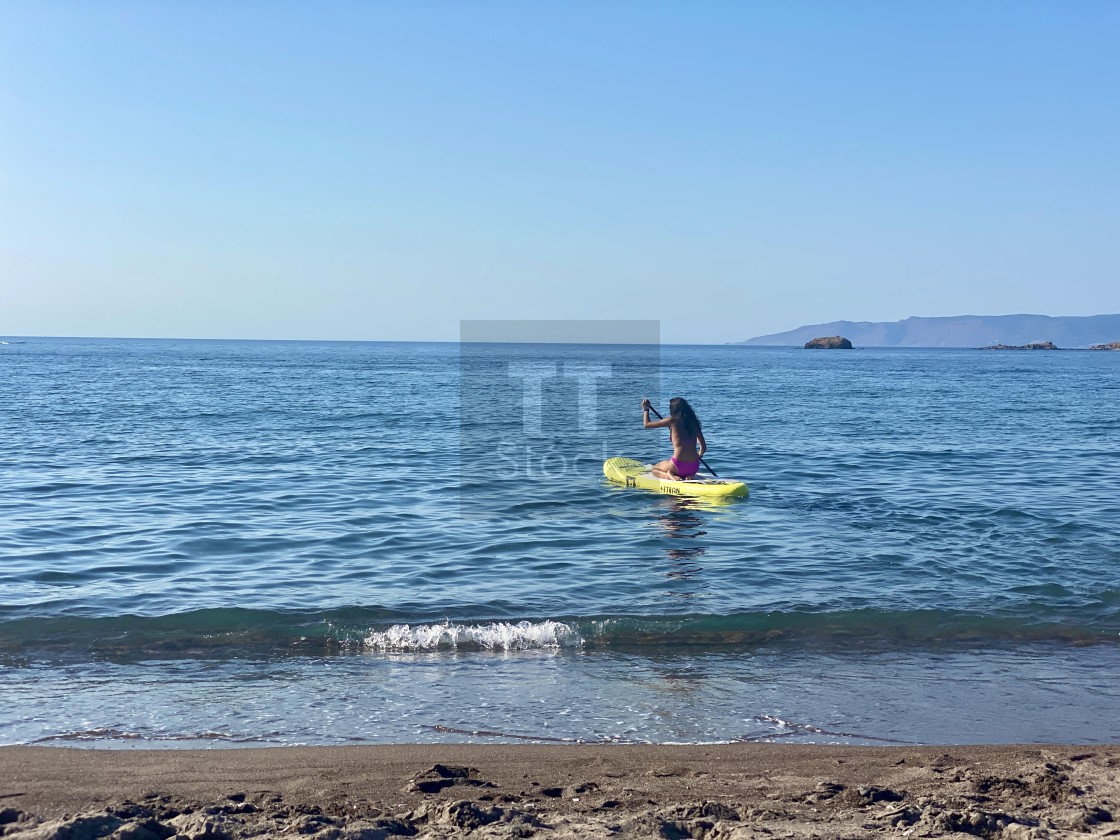 "Young woman wearing a pink bikini kneeling on a yellow sup board at sea." stock image