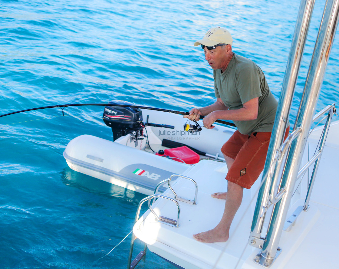 "A man catches a fish off the stern of his catamaran in the BVI." stock image