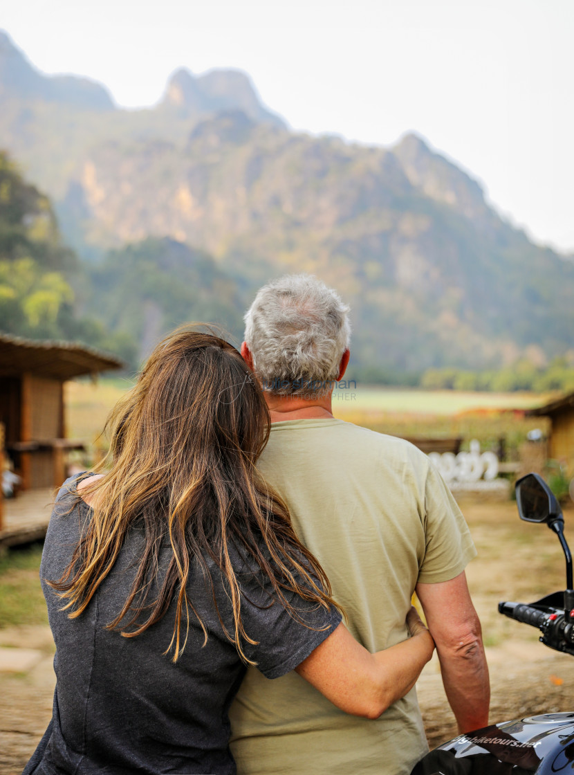 "A middle-aged couple sit together on a motocycle staring at a mountain in Thailand." stock image