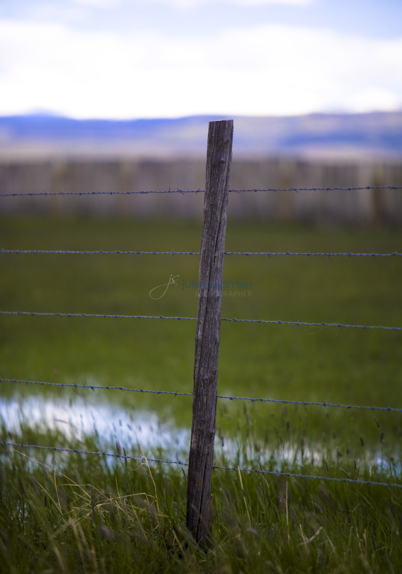 "A post of a barbed wire fence with layers of landscape behind in Robertson, Wyoming and the ranches in the Bridger Valley." stock image