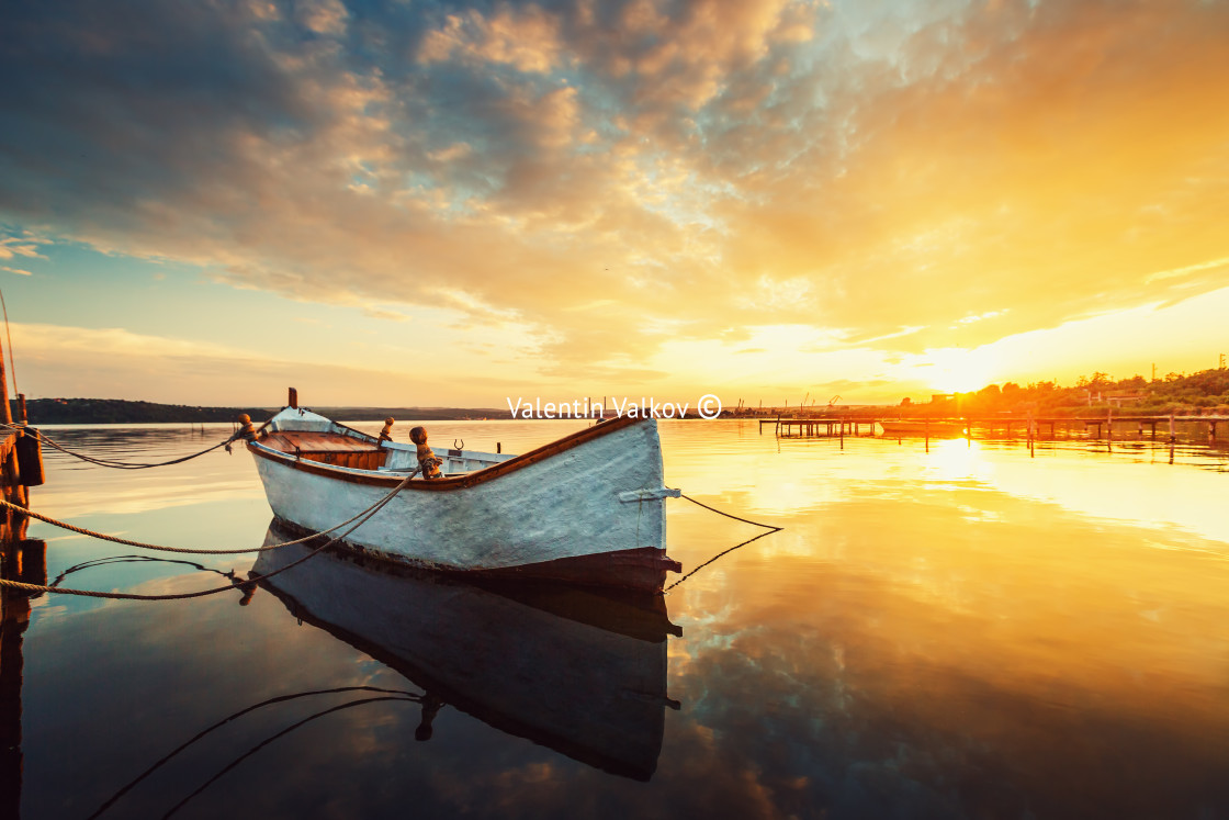 "Beautiful sunset over calm lake and a boat with sky reflecting in water" stock image