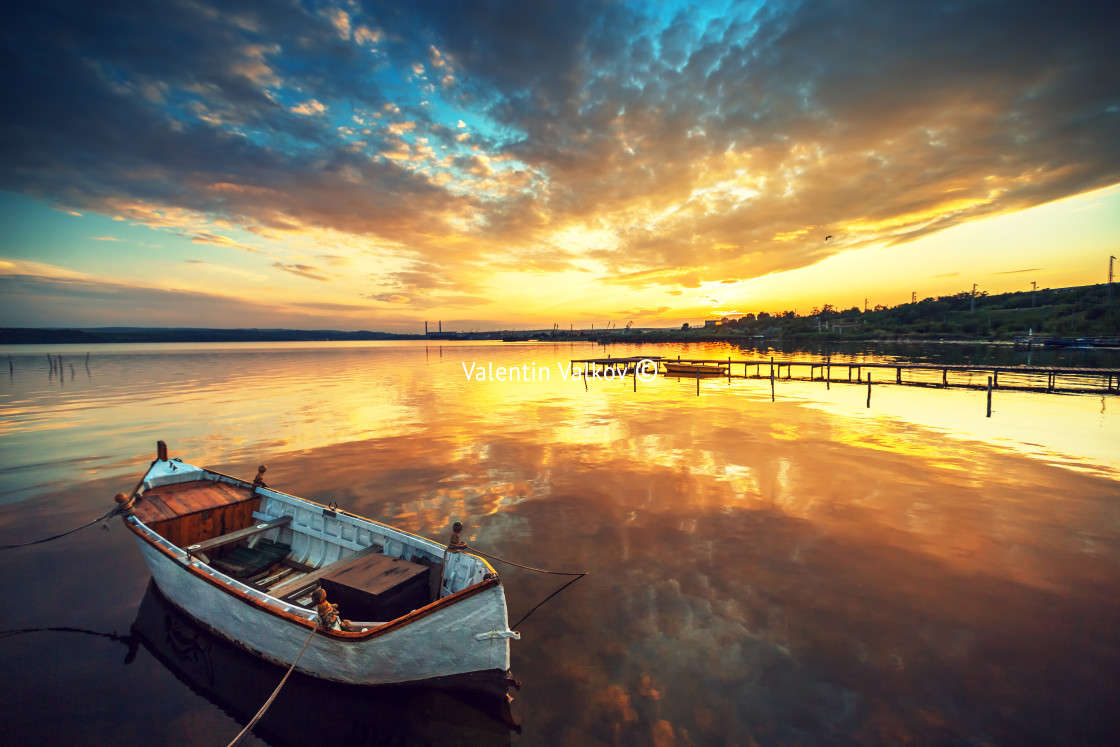 "Beautiful sunset over calm lake and a boat with sky reflecting in water" stock image