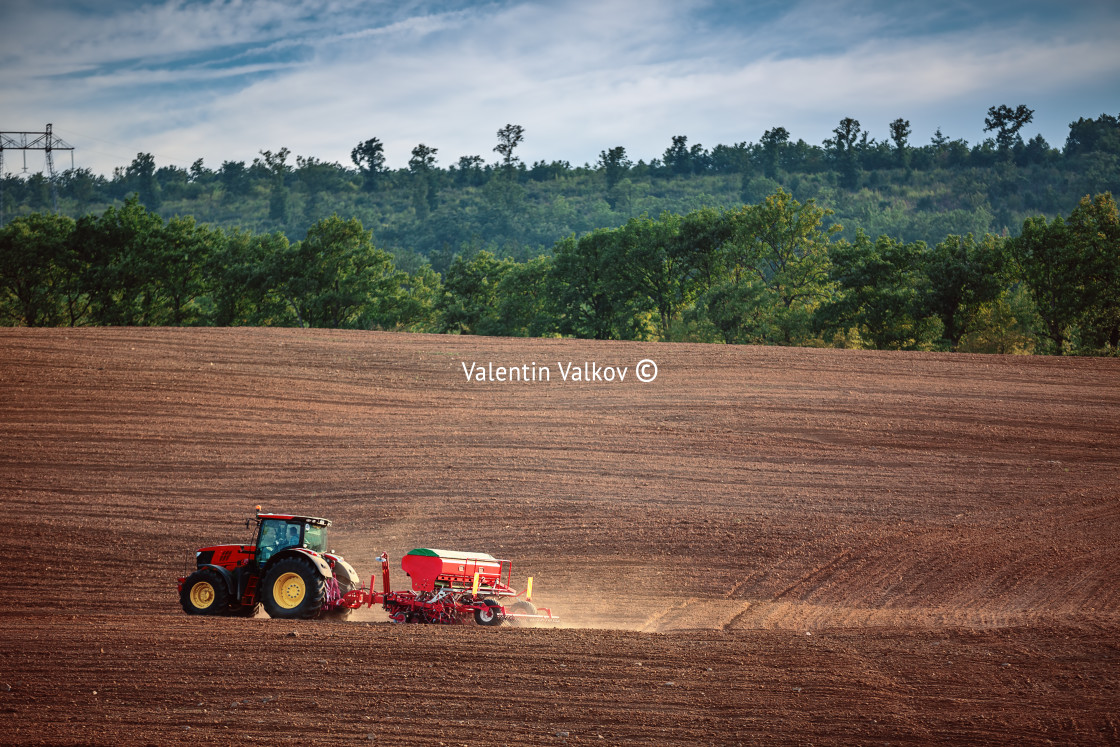 "Farmer with tractor seeding crops at field" stock image