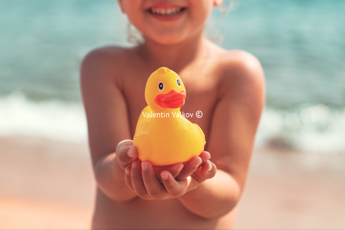 "Little girl holding in hands yellow rubber duck toy on the beach" stock image