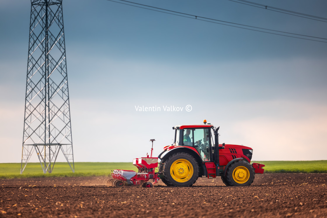 "Farmer with tractor seeding crops at field" stock image