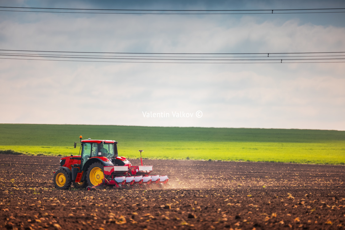 "Farmer with tractor seeding crops at field" stock image