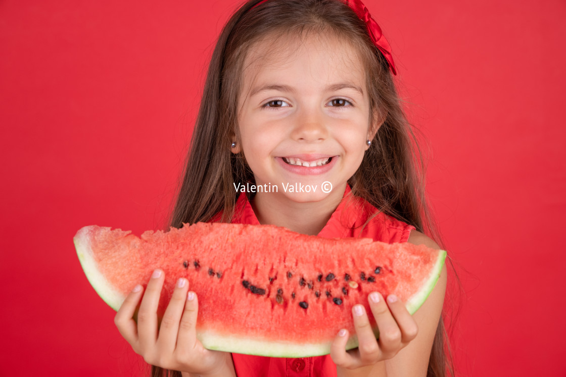 "Cute little girl holding, eating juicy slice of watermelon over" stock image